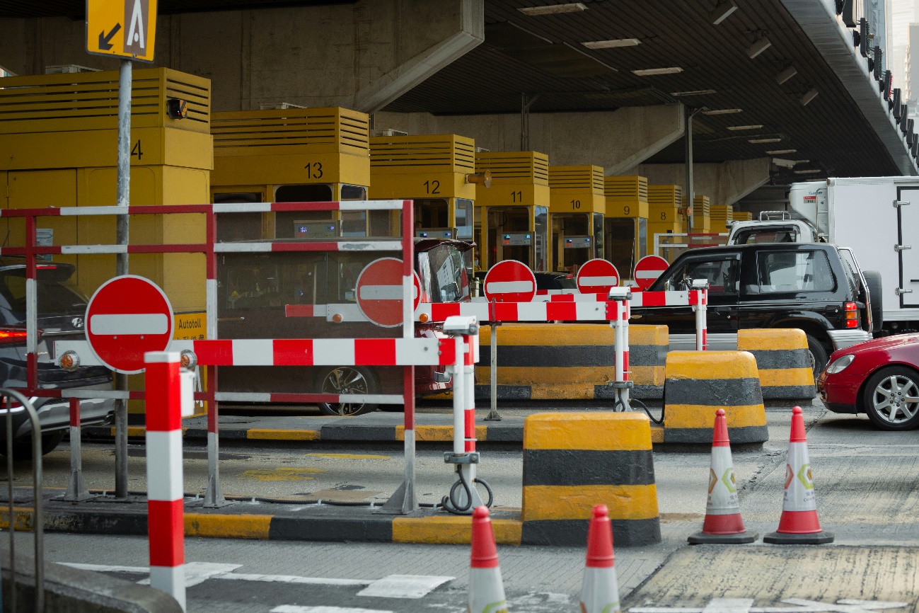 Image of a toll plaza with several numbered booths, where vehicles, including cars and a truck, are waiting to pay or pass