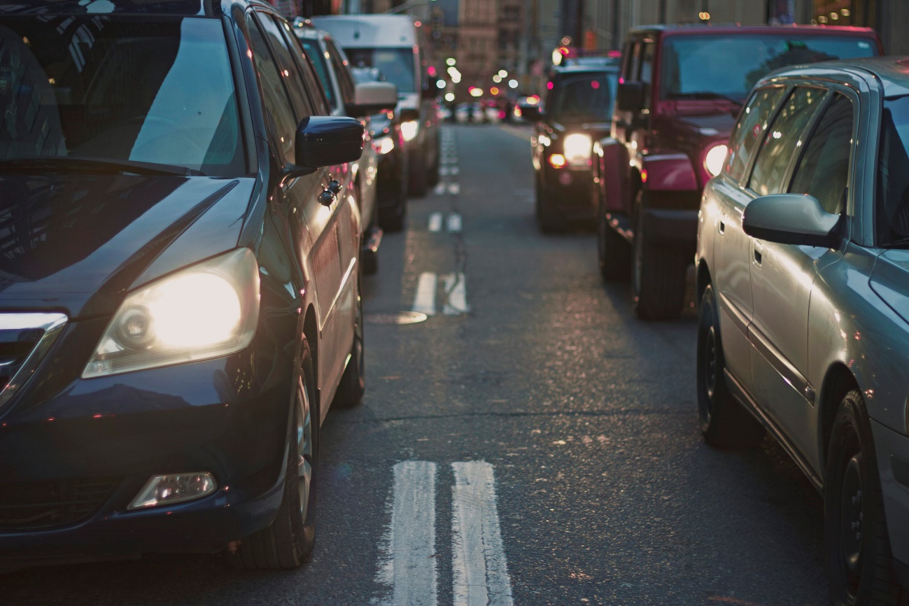 Photography of a dulled street with dusk, with several lit -aligned cars and headlights