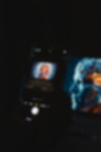 An iPhone that takes a photo of a MacBook. On the MacBook, you can see the head of a person who looks half a robot